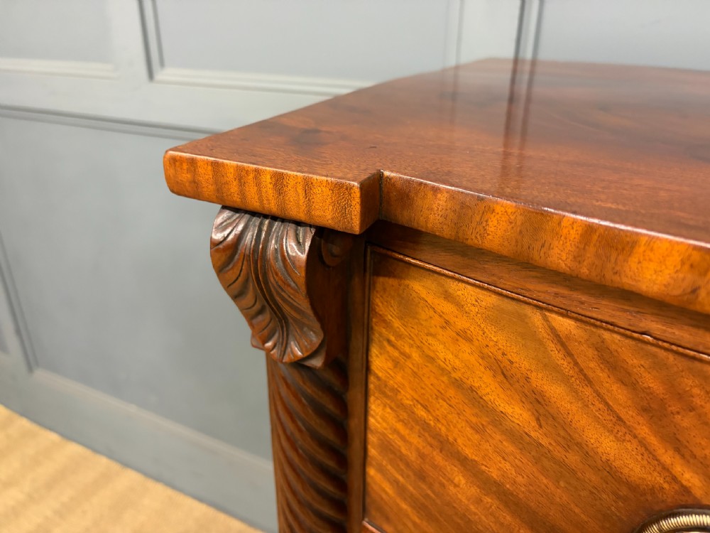 A Regency period mahogany bowfront chest of drawers featuring four graduated drawers, reeded side columns, brass ring handles, and turned feet. View VIII