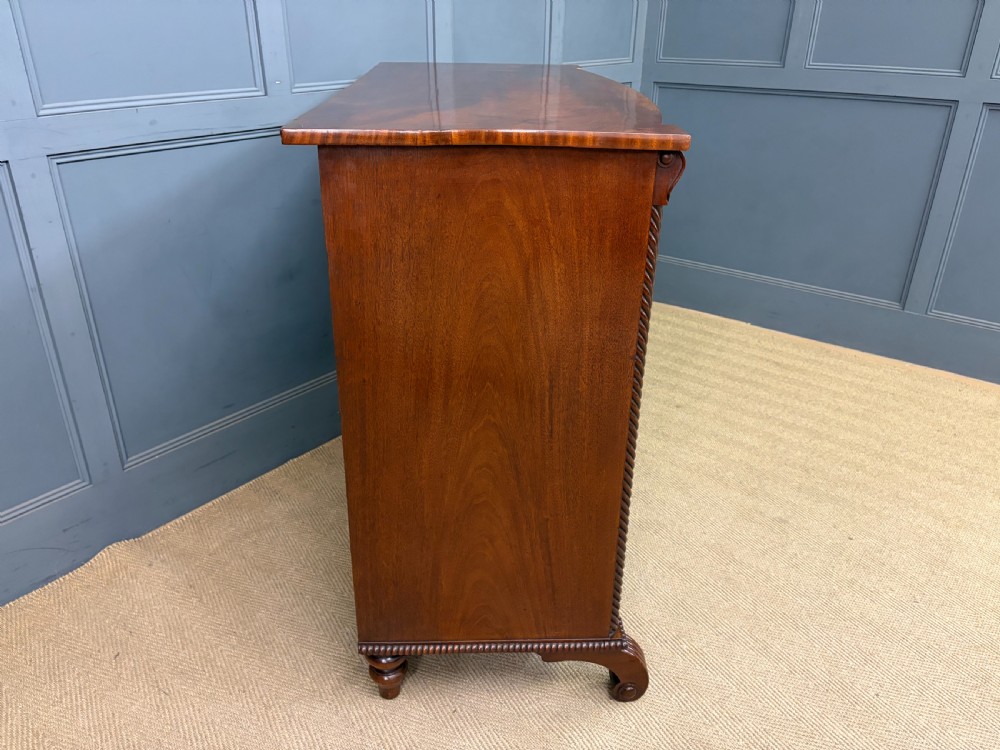 A Regency period mahogany bowfront chest of drawers featuring four graduated drawers, reeded side columns, brass ring handles, and turned feet. View XIII