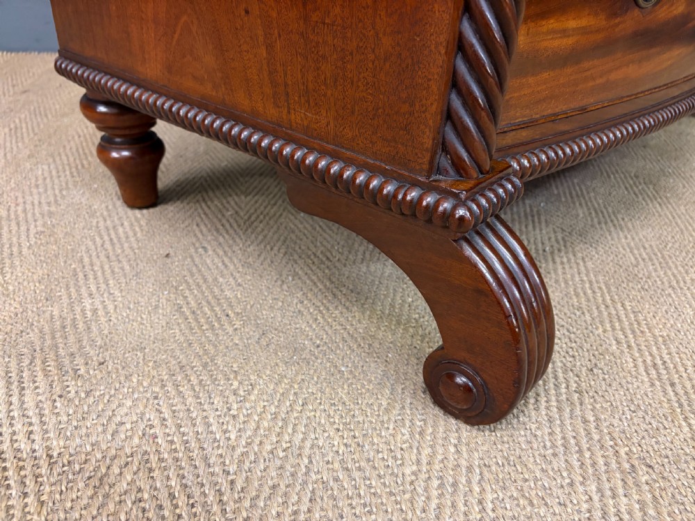 A Regency period mahogany bowfront chest of drawers featuring four graduated drawers, reeded side columns, brass ring handles, and turned feet. View XIV