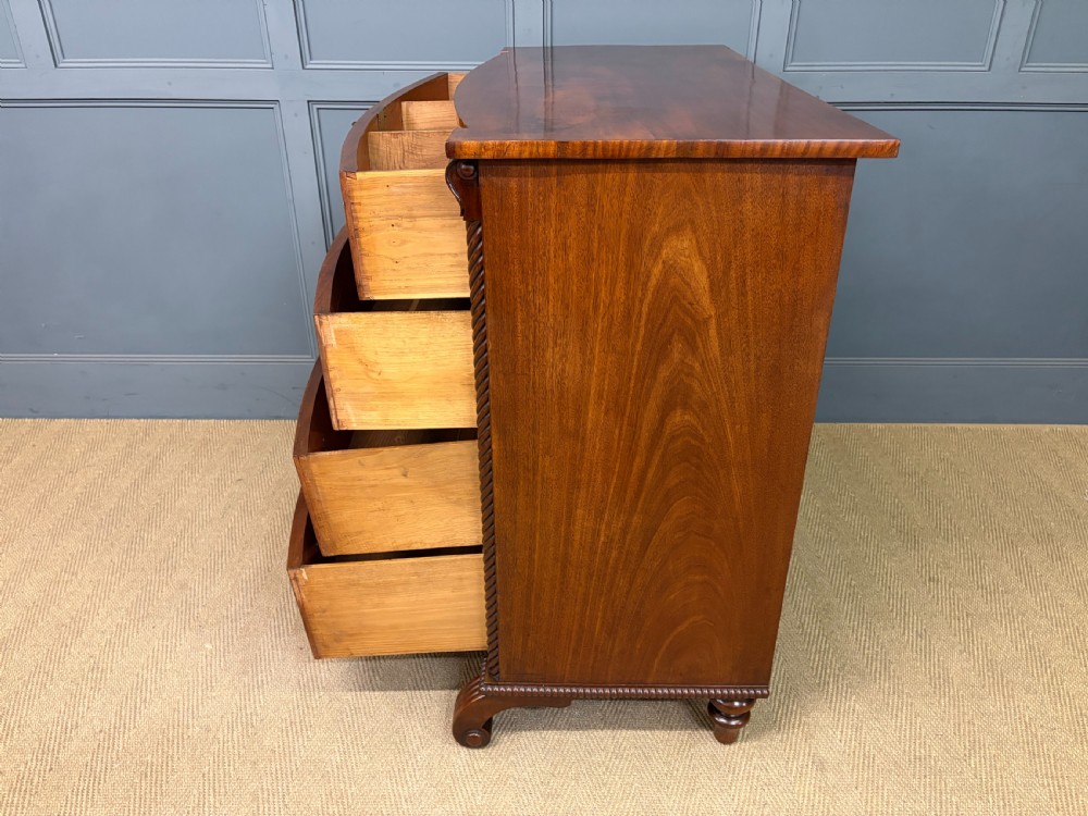 A Regency period mahogany bowfront chest of drawers featuring four graduated drawers, reeded side columns, brass ring handles, and turned feet. View XVIII