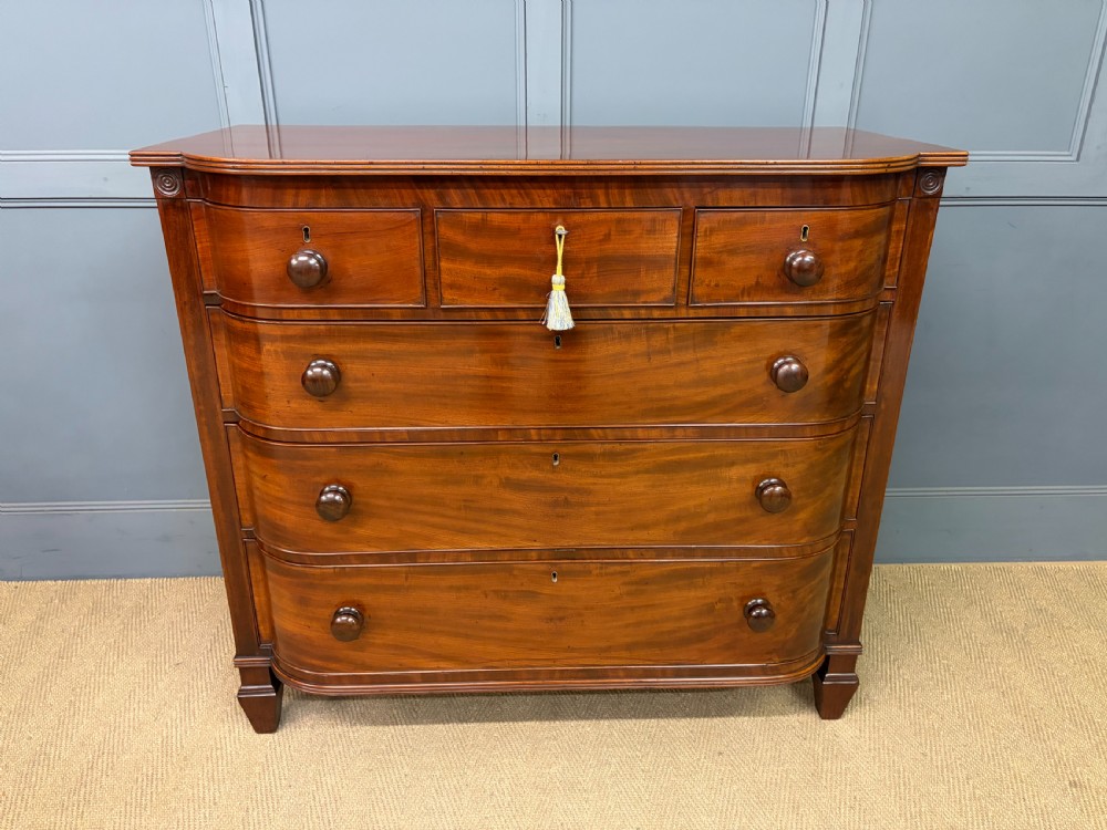A George IV flame mahogany chest of drawers featuring a bowfront profile, turned wooden handles, and carved side columns. View III