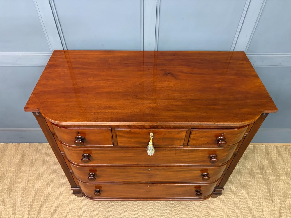 A George IV flame mahogany chest of drawers featuring a bowfront profile, turned wooden handles, and carved side columns. View V