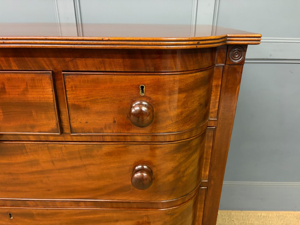 A George IV flame mahogany chest of drawers featuring a bowfront profile, turned wooden handles, and carved side columns. View VI