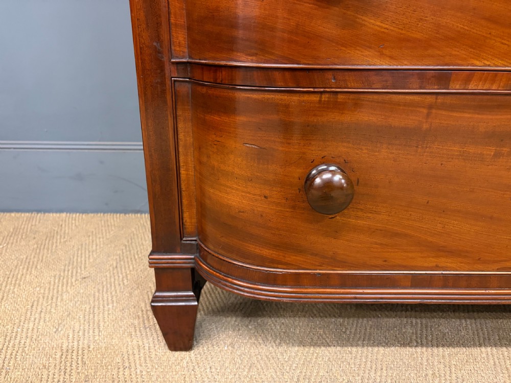 A George IV flame mahogany chest of drawers featuring a bowfront profile, turned wooden handles, and carved side columns. View VII