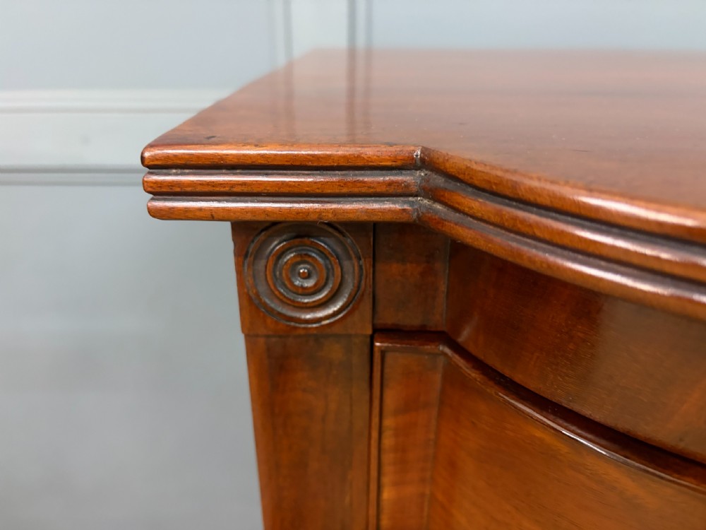 A George IV flame mahogany chest of drawers featuring a bowfront profile, turned wooden handles, and carved side columns. View VIII