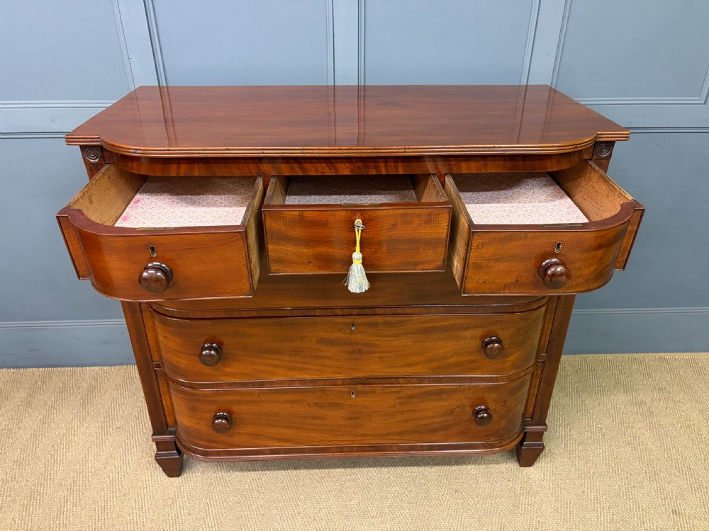 A George IV flame mahogany chest of drawers featuring a bowfront profile, turned wooden handles, and carved side columns. View IX