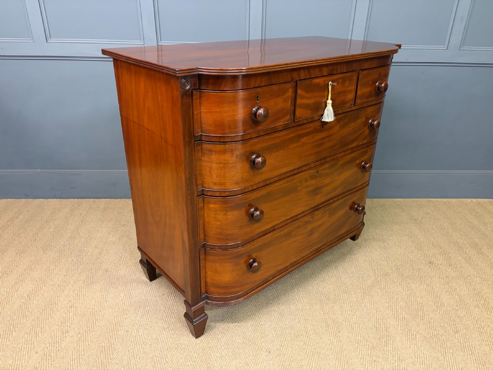A George IV flame mahogany chest of drawers featuring a bowfront profile, turned wooden handles, and carved side columns. View X