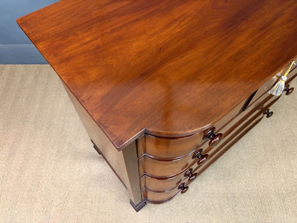 A George IV flame mahogany chest of drawers featuring a bowfront profile, turned wooden handles, and carved side columns. View XI