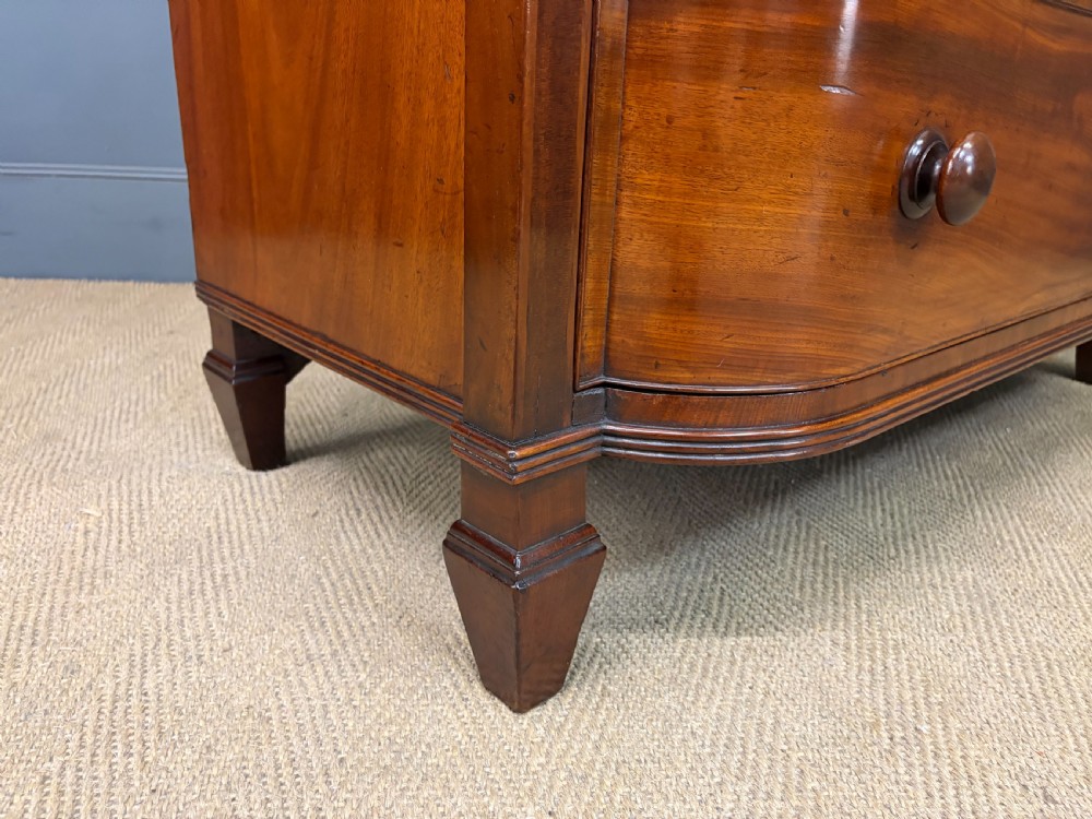 A George IV flame mahogany chest of drawers featuring a bowfront profile, turned wooden handles, and carved side columns. View XII