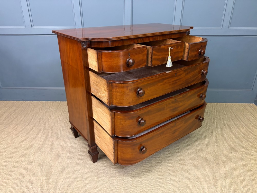 A George IV flame mahogany chest of drawers featuring a bowfront profile, turned wooden handles, and carved side columns. View XIV