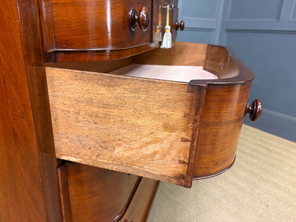 A George IV flame mahogany chest of drawers featuring a bowfront profile, turned wooden handles, and carved side columns. View XV