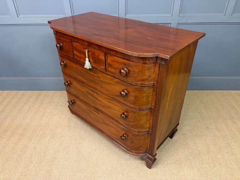 A George IV flame mahogany chest of drawers featuring a bowfront profile, turned wooden handles, and carved side columns. View XVI