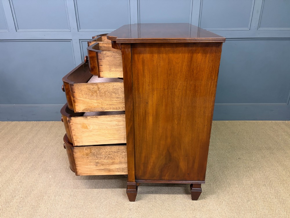 A George IV flame mahogany chest of drawers featuring a bowfront profile, turned wooden handles, and carved side columns. View XVII