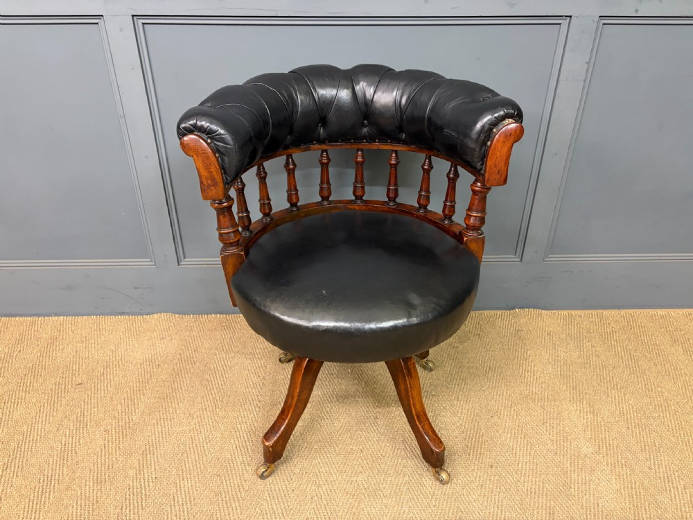 Victorian mahogany revolving desk chair featuring a deep button-tufted black leather curved back, turned spindles, a circular leather seat, and a swivel quadruped base with brass castors. View III