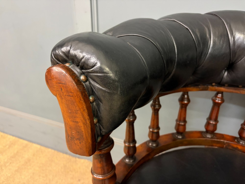 Victorian mahogany revolving desk chair featuring a deep button-tufted black leather curved back, turned spindles, a circular leather seat, and a swivel quadruped base with brass castors. View VI