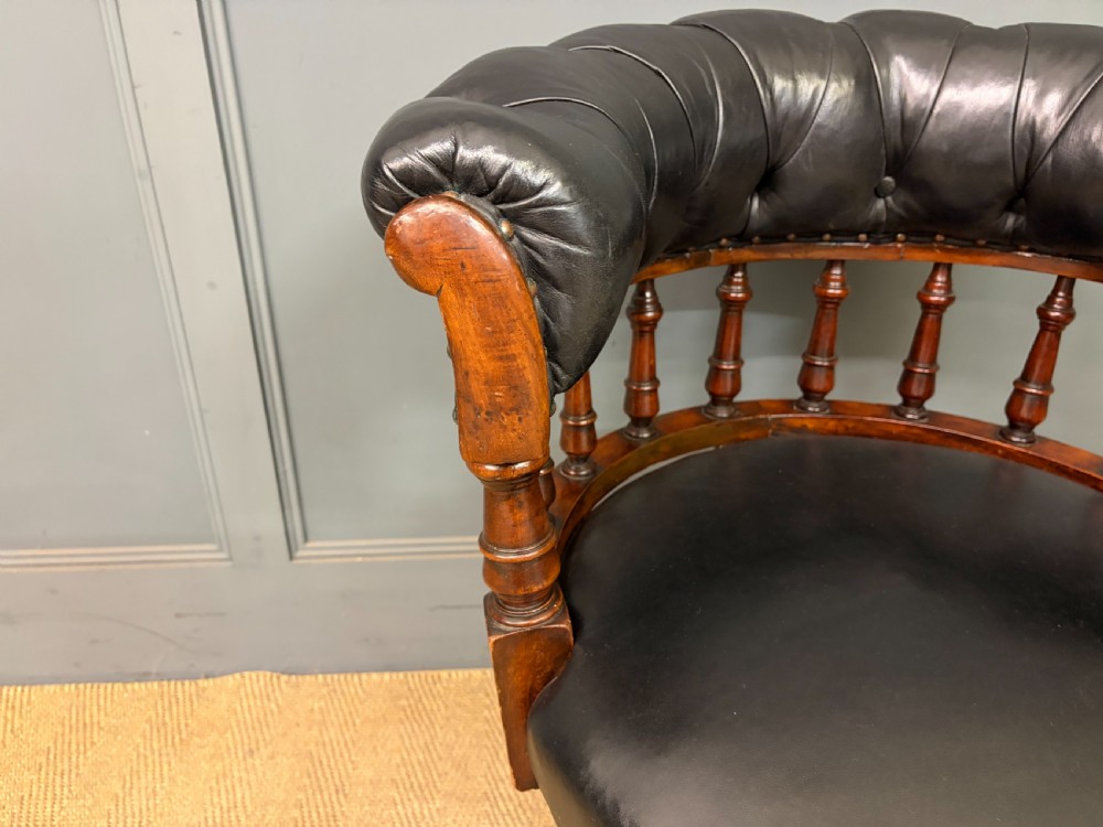 Victorian mahogany revolving desk chair featuring a deep button-tufted black leather curved back, turned spindles, a circular leather seat, and a swivel quadruped base with brass castors. View VII