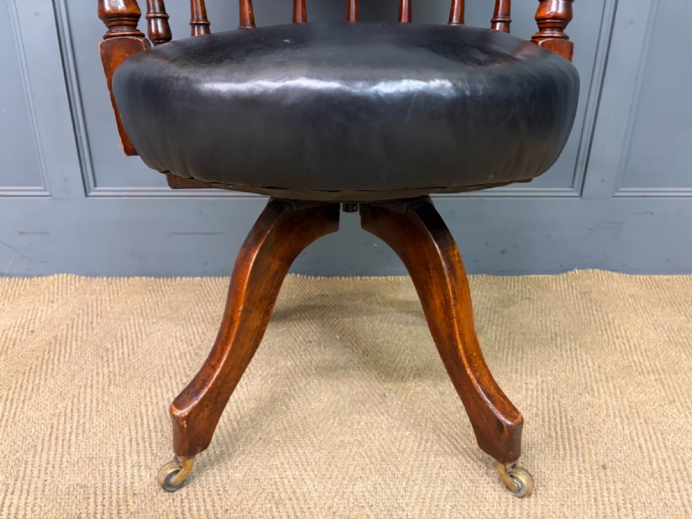Victorian mahogany revolving desk chair featuring a deep button-tufted black leather curved back, turned spindles, a circular leather seat, and a swivel quadruped base with brass castors. View VIII