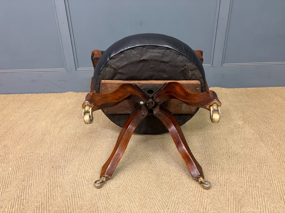 Victorian mahogany revolving desk chair featuring a deep button-tufted black leather curved back, turned spindles, a circular leather seat, and a swivel quadruped base with brass castors. View XII