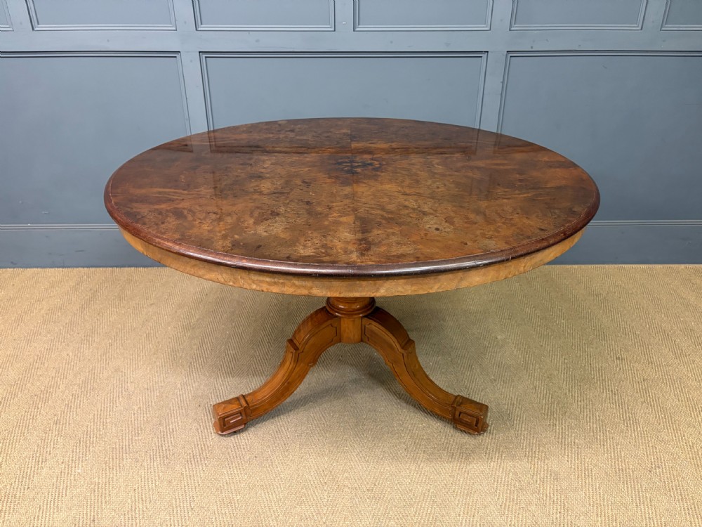 A circular burr walnut centre table featuring a quartered figured veneer top over a turned central pedestal with four carved scroll legs. View VI