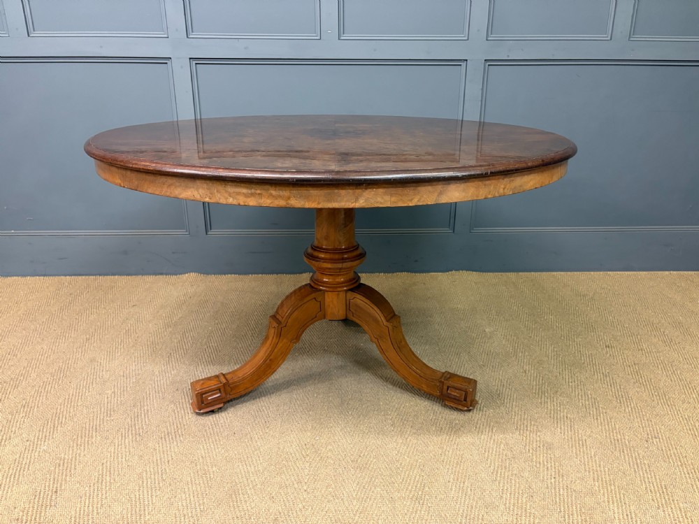 A circular burr walnut centre table featuring a quartered figured veneer top over a turned central pedestal with four carved scroll legs. View VII