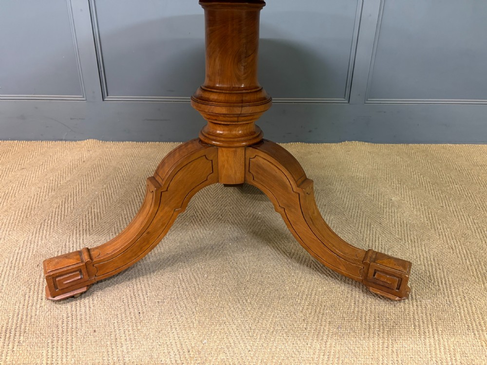 A circular burr walnut centre table featuring a quartered figured veneer top over a turned central pedestal with four carved scroll legs. View X