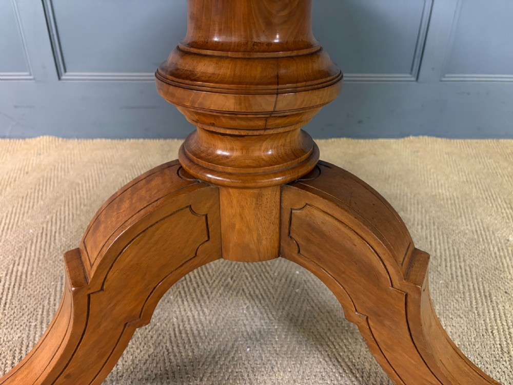A circular burr walnut centre table featuring a quartered figured veneer top over a turned central pedestal with four carved scroll legs. View XII