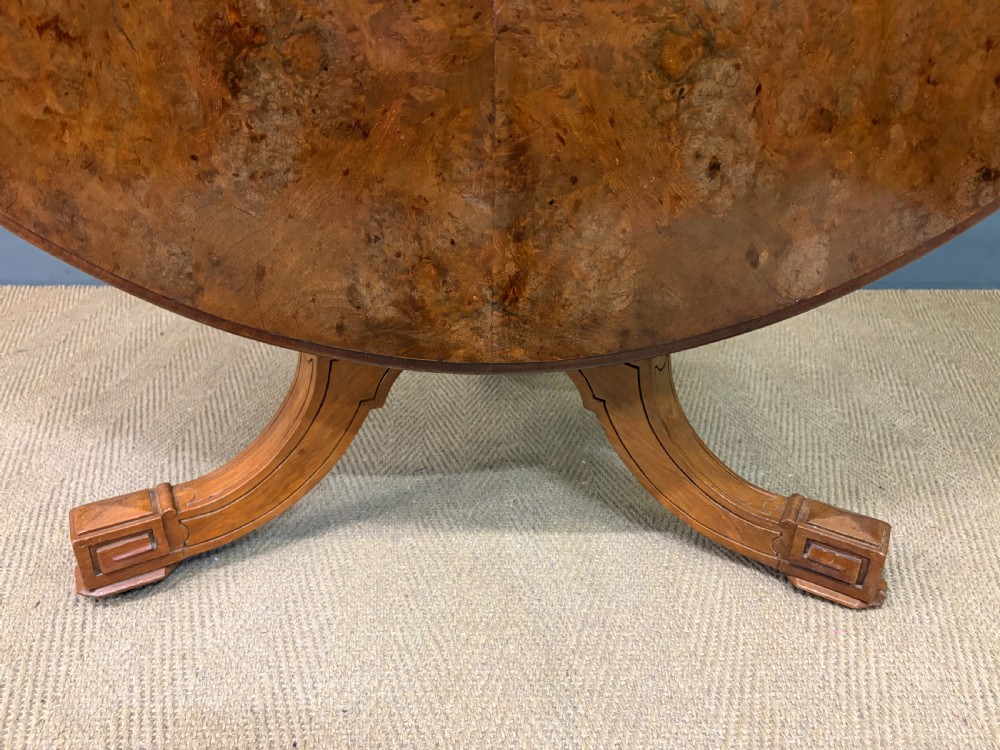 A circular burr walnut centre table featuring a quartered figured veneer top over a turned central pedestal with four carved scroll legs. View XV