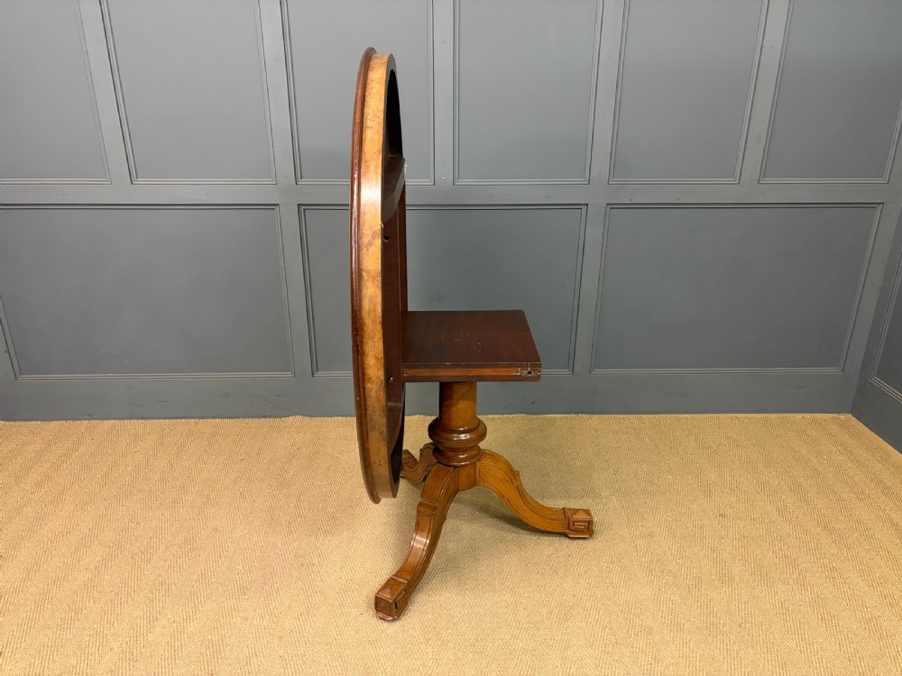 A circular burr walnut centre table featuring a quartered figured veneer top over a turned central pedestal with four carved scroll legs. View XVIII