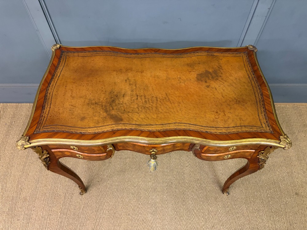 A 19th-century French Louis XV style writing desk with geometric parquetry veneers, gilt-bronze mounts, cabriole legs, and a warm brown leather writing surface. View IV
