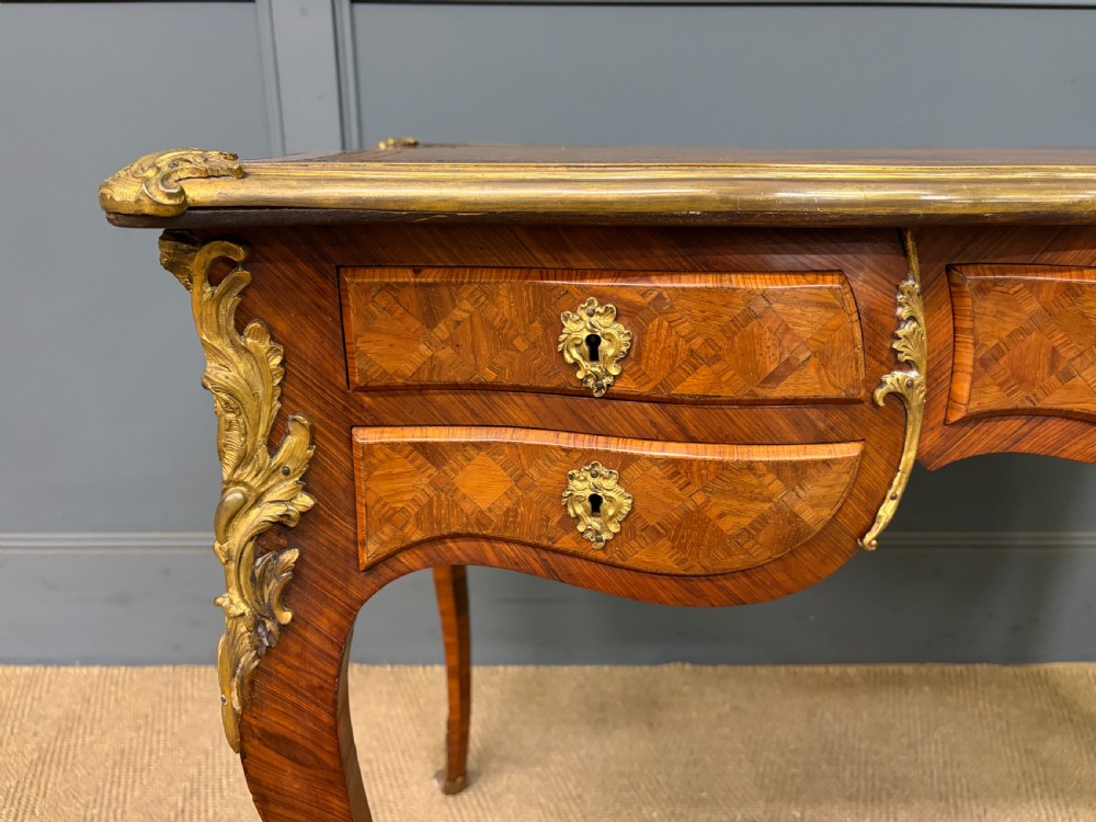A 19th-century French Louis XV style writing desk with geometric parquetry veneers, gilt-bronze mounts, cabriole legs, and a warm brown leather writing surface. View VI