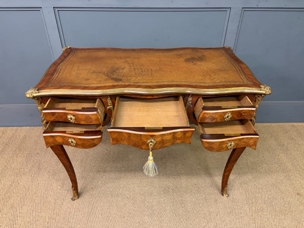 A 19th-century French Louis XV style writing desk with geometric parquetry veneers, gilt-bronze mounts, cabriole legs, and a warm brown leather writing surface. View IX