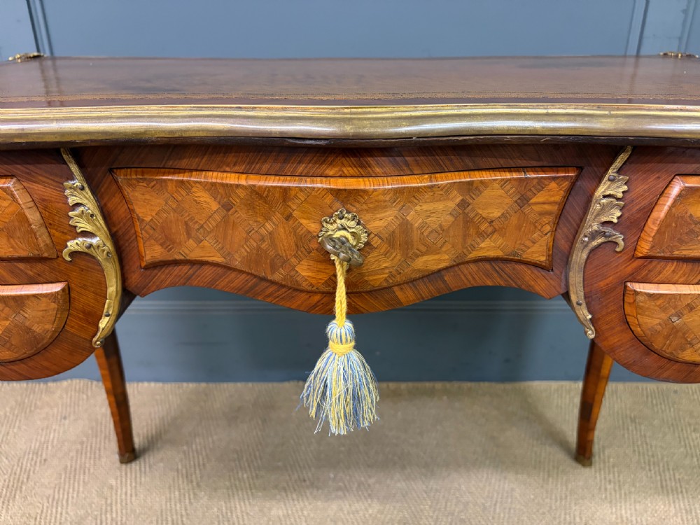 A 19th-century French Louis XV style writing desk with geometric parquetry veneers, gilt-bronze mounts, cabriole legs, and a warm brown leather writing surface. View XI