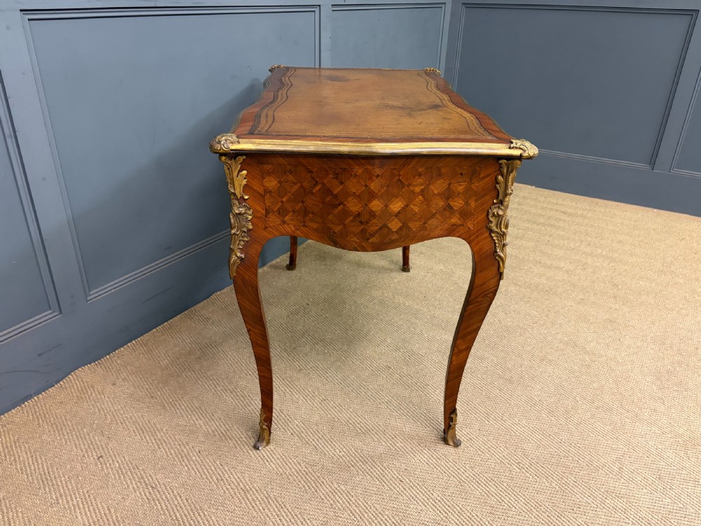 A 19th-century French Louis XV style writing desk with geometric parquetry veneers, gilt-bronze mounts, cabriole legs, and a warm brown leather writing surface. View XV