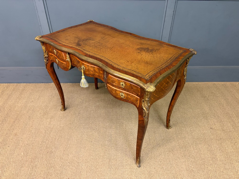 A 19th-century French Louis XV style writing desk with geometric parquetry veneers, gilt-bronze mounts, cabriole legs, and a warm brown leather writing surface. View XVIII