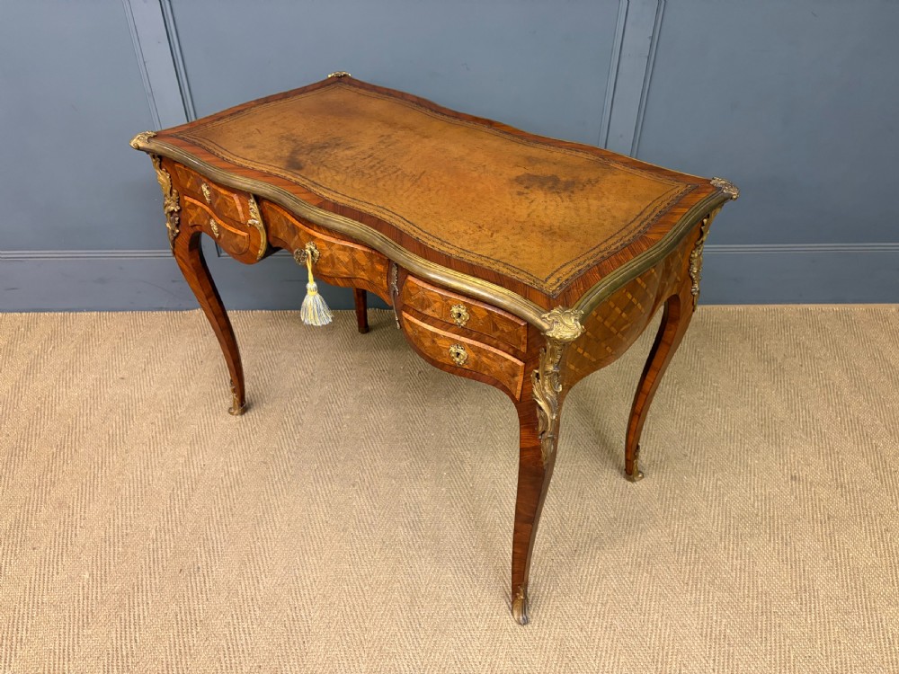 A 19th-century French Louis XV style writing desk with geometric parquetry veneers, gilt-bronze mounts, cabriole legs, and a warm brown leather writing surface. View XIX