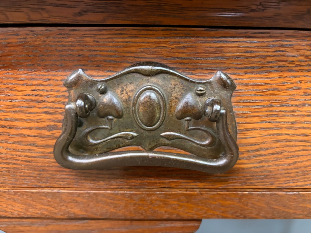 An Arts and Crafts period oak writing desk featuring an inset green leather top, single frieze drawer with brass handles, and pierced side supports. View VII