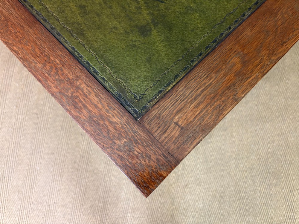 An Arts and Crafts period oak writing desk featuring an inset green leather top, single frieze drawer with brass handles, and pierced side supports. View XV