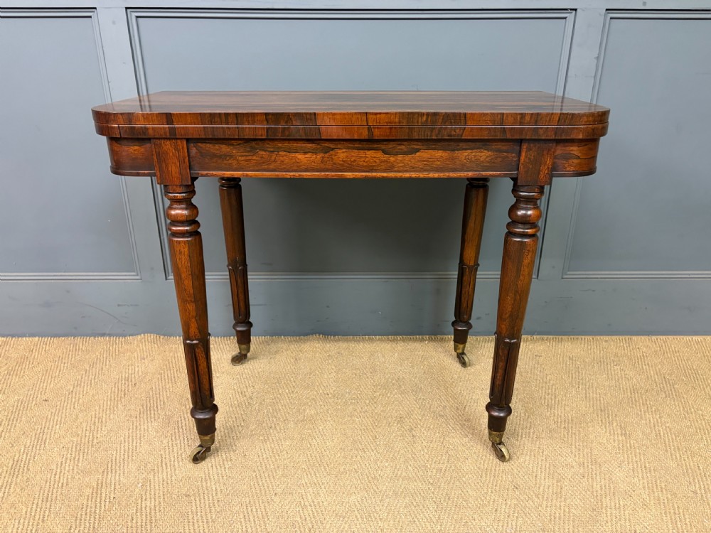An early Victorian rosewood card table featuring a figured fold-over top, rectangular apron, turned tapered legs, and original brass castors. View VI