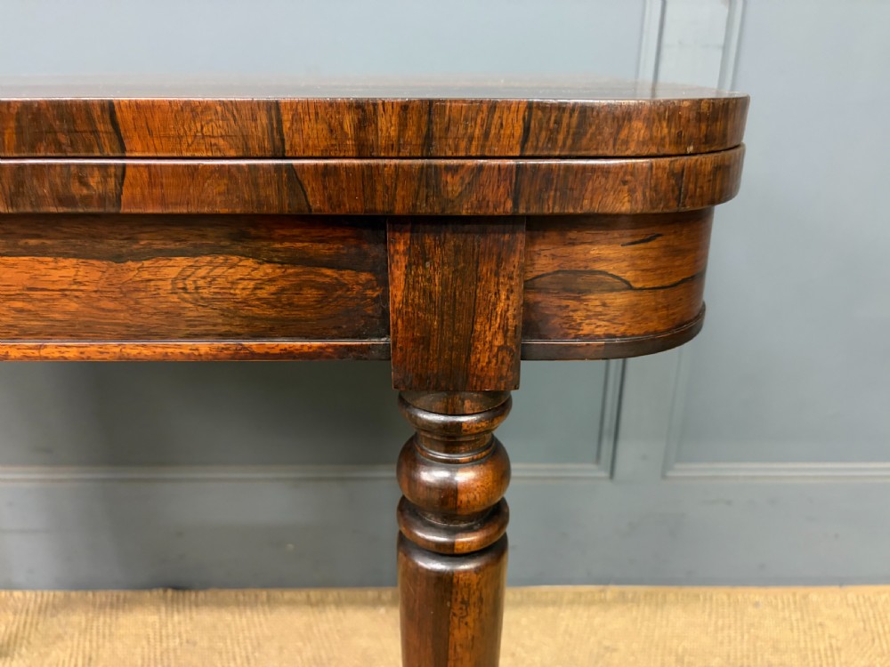 An early Victorian rosewood card table featuring a figured fold-over top, rectangular apron, turned tapered legs, and original brass castors. View VII
