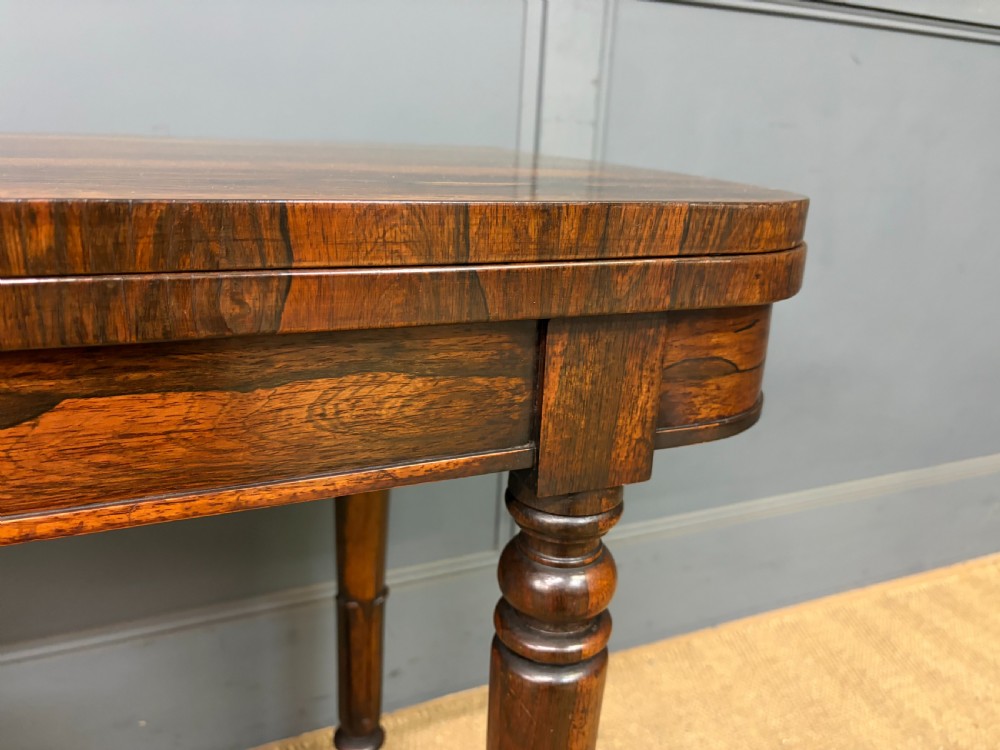 An early Victorian rosewood card table featuring a figured fold-over top, rectangular apron, turned tapered legs, and original brass castors. View VIII