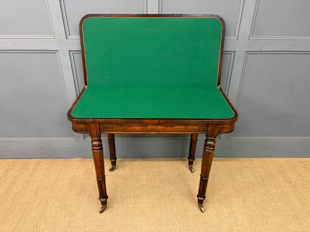 An early Victorian rosewood card table featuring a figured fold-over top, rectangular apron, turned tapered legs, and original brass castors. View IX