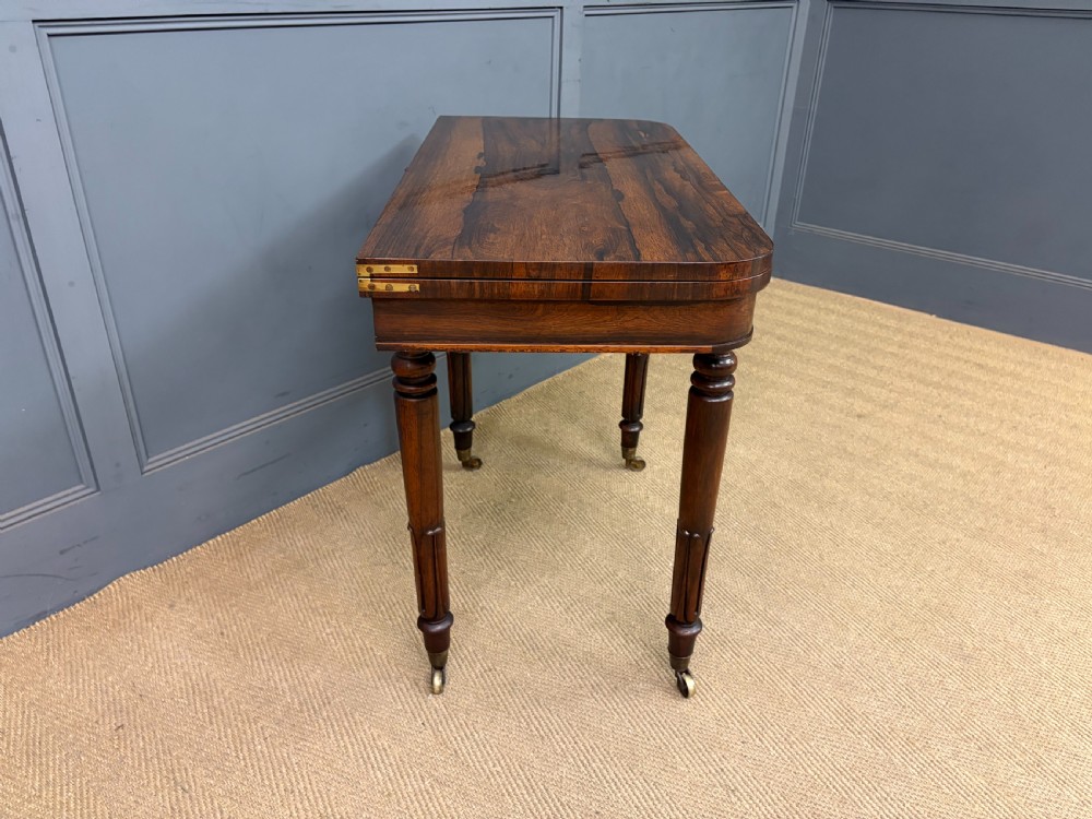 An early Victorian rosewood card table featuring a figured fold-over top, rectangular apron, turned tapered legs, and original brass castors. View XII