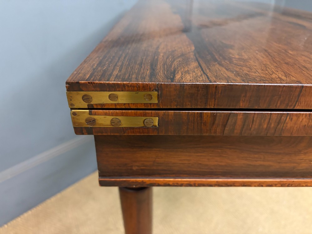 An early Victorian rosewood card table featuring a figured fold-over top, rectangular apron, turned tapered legs, and original brass castors. View XIII