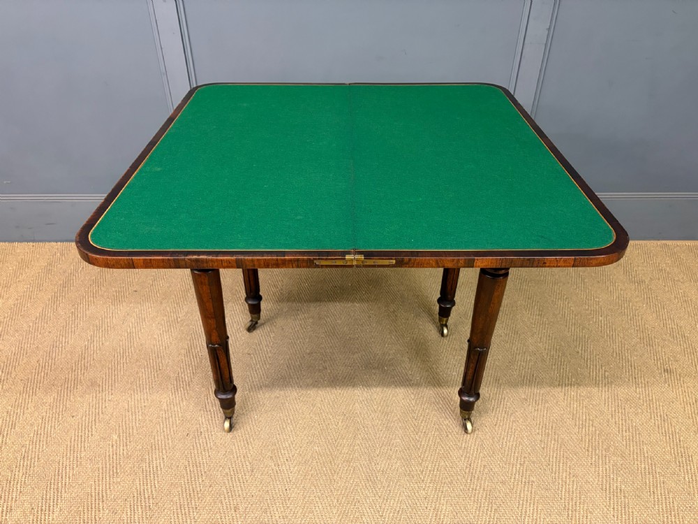 An early Victorian rosewood card table featuring a figured fold-over top, rectangular apron, turned tapered legs, and original brass castors. View XIV