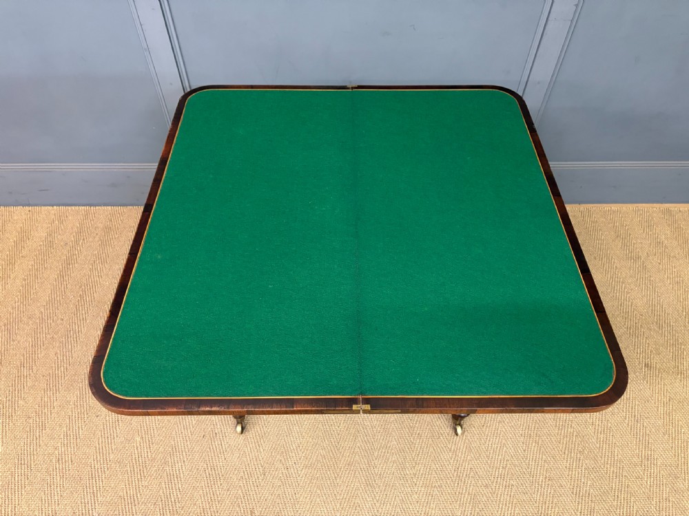 An early Victorian rosewood card table featuring a figured fold-over top, rectangular apron, turned tapered legs, and original brass castors. View XV