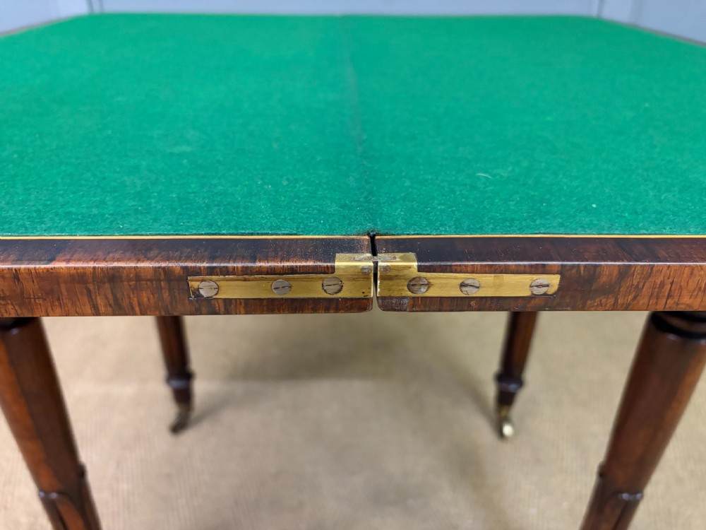 An early Victorian rosewood card table featuring a figured fold-over top, rectangular apron, turned tapered legs, and original brass castors. View XVI