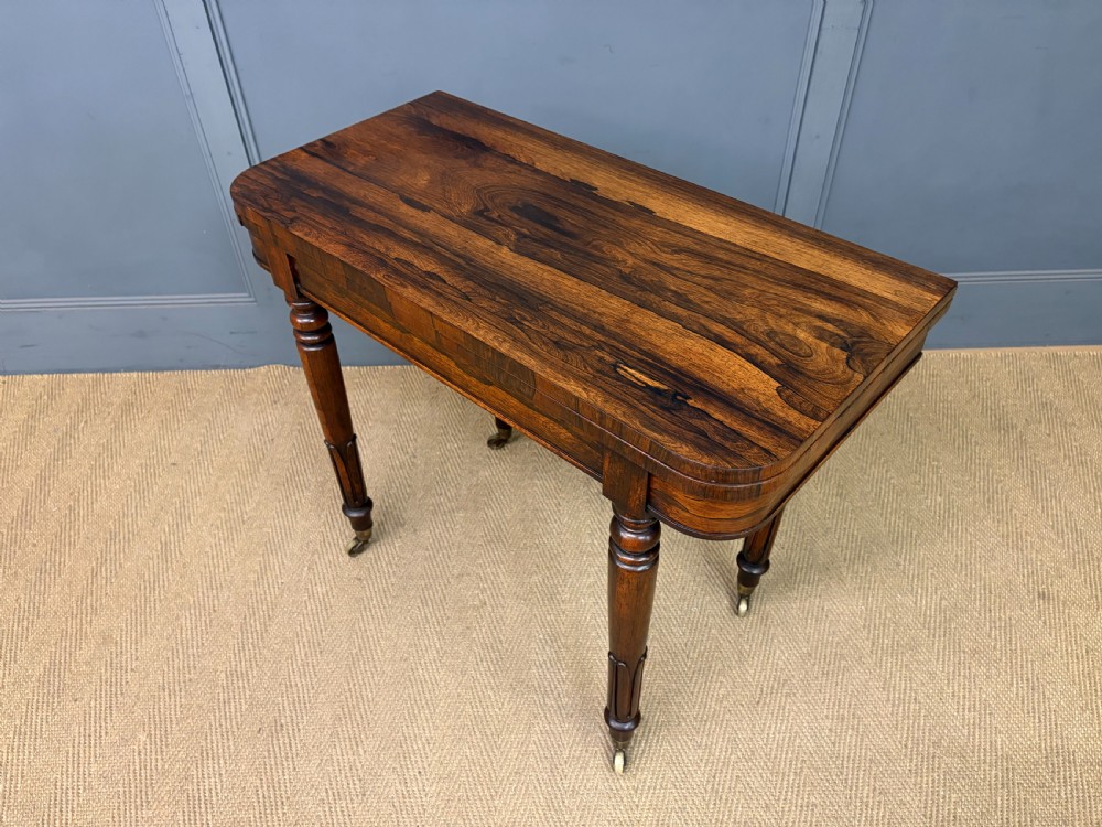 An early Victorian rosewood card table featuring a figured fold-over top, rectangular apron, turned tapered legs, and original brass castors. View XX