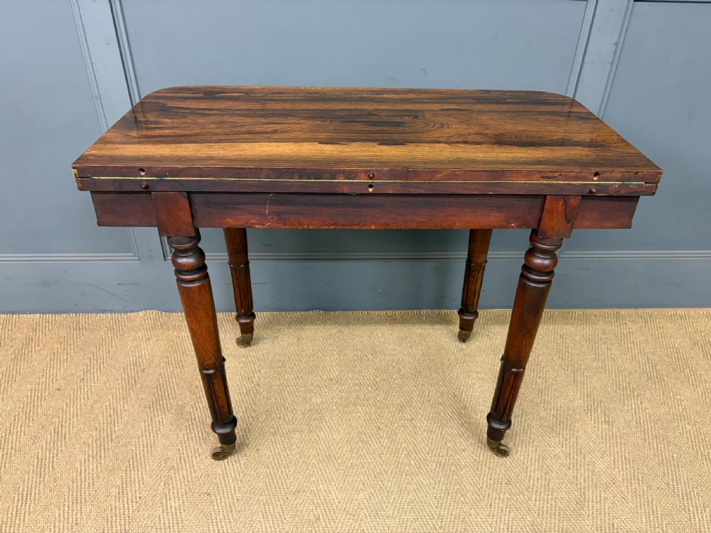 An early Victorian rosewood card table featuring a figured fold-over top, rectangular apron, turned tapered legs, and original brass castors. View XXI