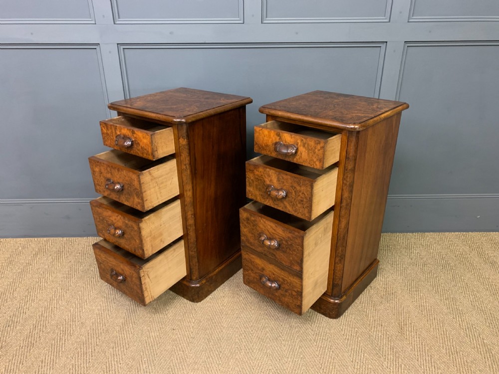 A pair of narrow Victorian burr walnut bedside chests featuring four drawers each with carved wooden handles and plinth bases. View VIII