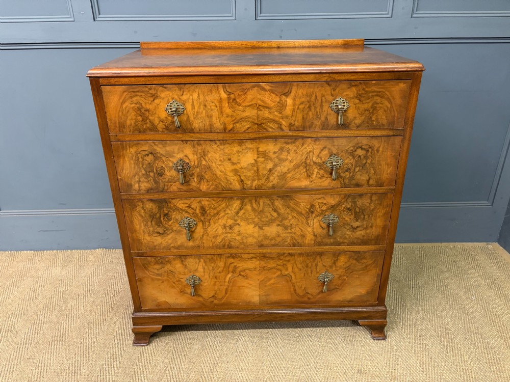 An Art Deco burr walnut chest of four full-width drawers featuring figured veneer panels, decorative brass drop handles, and low bracket feet.